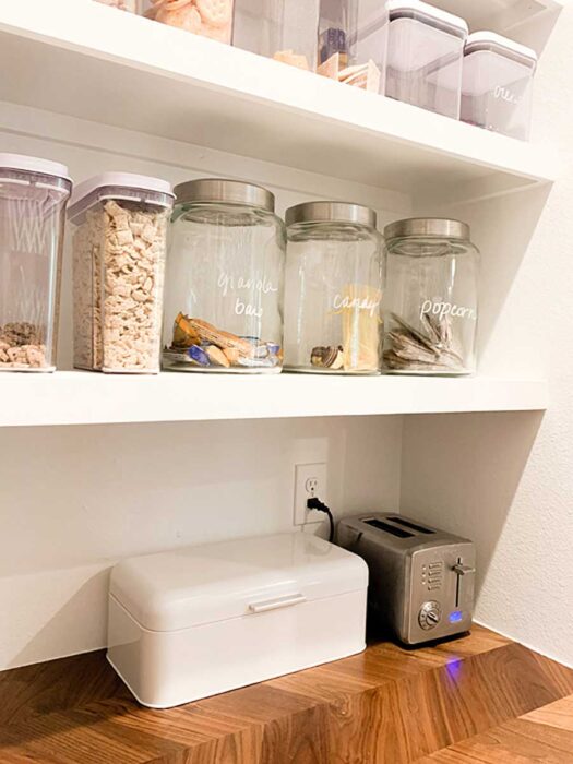 How I Organize My Walk-In Farmhouse Pantry with a bread box and toaster on the workspace inside. Plus, large glass jars for bulk snacks.